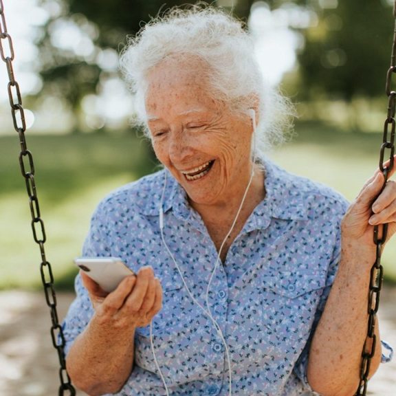 Eine lächelnde Seniorin auf einer Schaukel im Grünen